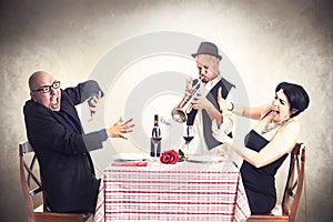 Angry couple disturbed by a trumpet musician while having dinner photo
