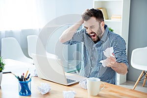 Angry crazy bearded businessman yelling and crumpling paper on his workplace