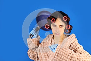 Angry crazy housewife in curlers with a frying pan on a blue background