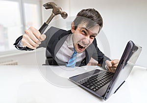 Angry and crazy man is working with laptop. He is going to damage notebook with hammer