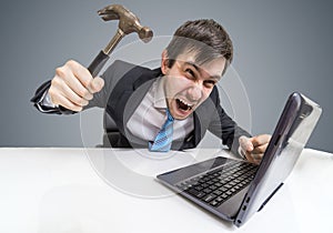 Angry and crazy man is working with laptop. He is going to damage notebook with hammer