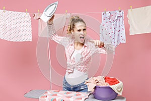 Angry crazy woman housewife in checkered shirt dry clothes on rope ironing clean clothes on board doing housework