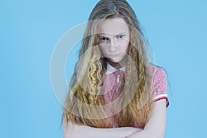 Angry Cruel Teenager Girl in Red Checked Dress With Folded Hands Against Blue Background