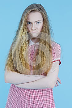 Angry Cruel Teenager Girl in Red Checked Dress With Folded Hands Against Blue Background