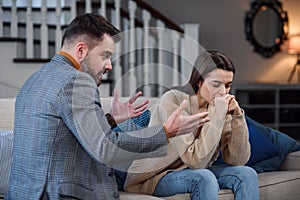 Upset man at table and woman with shopping bags in room. Money problems in relationship