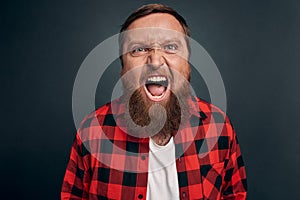 Angry and disappointed handsome bearded man in checkered shirt swearing and cursing everyone as lost bid, shaking hands outraged