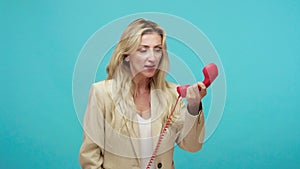 Angry displeased adult woman with blond hair in business style jacket, loudly screaming holding in hand landline phone
