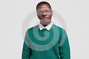 Angry dissatisfied black man frowns face has disappointed facial expression, vexed look, dressed in green jumper