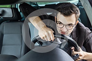 Angry driver is looking through the windsheeld. He is driving his car and holding steering wheel with both hands