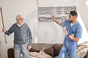 Angry elderly person threatening his caregiver with his cane