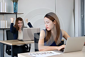 Angry envious Asian business woman looking successful competitor colleague in office.