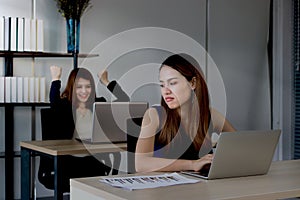 Angry envious Asian business woman looking successful competitor colleague in office. Low key toned image