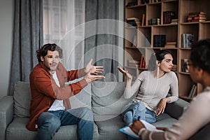 Angry excited young european man swearing at wife on family consultation in clinic interior