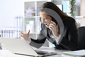 Angry executive calling on phone looking at laptop at office