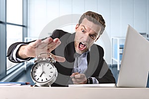 Angry exploited businessman at office desk stressed and frustrated with computer laptop and alarm clock