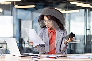 Angry female accountant holding document and calculator in hand while working in office settings. Shocked black woman in