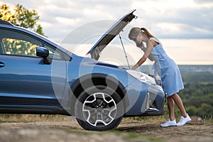 Angry female driver speaking angrily on cell phone with assistance service worker standing near a broken car with popped up hood