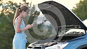 Angry female driver speaking angrily on cell phone with assistance service worker standing near a broken car with popped up hood w