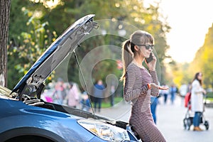 Angry female driver talking on cell phone with assistance service worker standing near a broken car