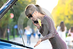 Angry female driver talking on cell phone with assistance service worker standing near a broken car with popped up hood