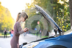 Angry female driver talking on cell phone with assistance service worker standing near a broken car with popped up hood on road