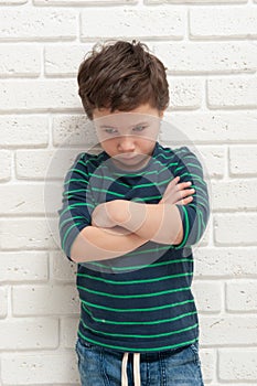 Angry frowning boy on brick wall background.