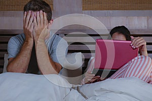 Angry and frustrated husband moody in bed ignored by his workaholic wife or internet social media addict girlfriend using laptop