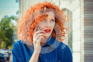 Angry frustrated, red curly hair woman talking on mobile phone standing outside