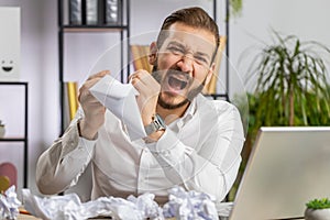 Angry furious man working at home office throwing crumpled paper, having nervous breakdown at work