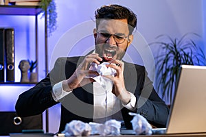 Angry furious man working at home office throwing crumpled paper, having nervous breakdown at work