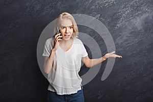 Angry girl arguing by mobile at black studio background