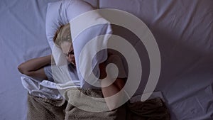 Angry girl closing ears with pillow, noisy neighbors disturbing sleep at night