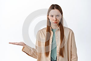 Angry girl frowning, holding in open hand over copyspace, showing item on palm against copyspace, looking with anger and