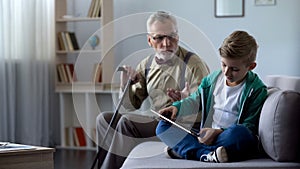 Angry grandpa scolding grandson for playing video game on tablet, generation gap