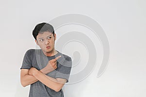 Angry and hate face of young Asian man in gray t-shirt with hand point on empty space