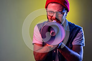 Angry hipster man holding megaphone near mouth loudly speaking, screaming, making announcement.