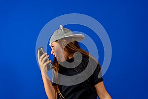 Angry Little girl with beautiful brunette hair over blue background screaming on the phone, having an argument.