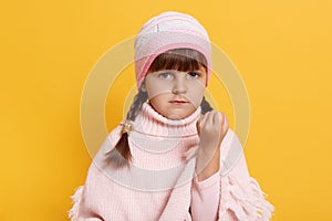 Angry little girl isolated over yellow background, showing fist to camera, having aggressive facial expression, wearing pink