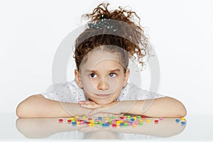 Angry little girl looking at candy, hesitate to eat, sitting at the table on a white background.