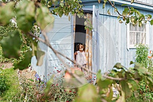 Angry little girl peeking out the door of a village old house