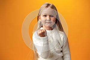 Angry little girl showing fist at the camera against yellow background