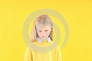 Angry little girl in sweater on yellow background