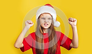 Angry little girl wearing Christmas hat standing isolated over yellow background wall in studio