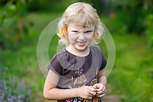 Angry little girl writhing her face in the park on the background of green grass. Portrait of a cute little girl with