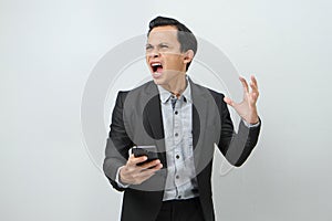 angry mad asian indonesian business man in suit holding smart phone on isolated background