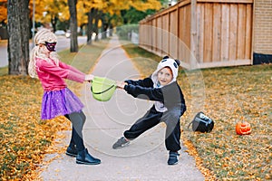 Angry mad children fighting for basket. Funny trick or treat on Halloween holiday. Kids boy and girl friends in party costumes can