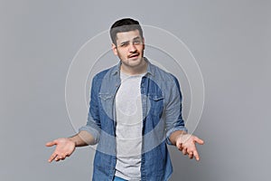 Angry mad sad upset unshaven young man in denim jeans shirt posing isolated on grey wall background studio portrait