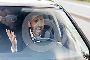 Angry male car driver yells at other drivers and pedestrians who obstruct traffic, mature adult businessman in a