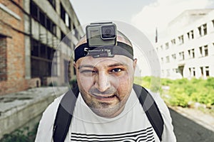 Angry man with action camera on head looking at camera and go. Portrait of travel blogger in urban background