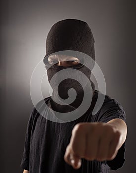 Angry man in a balaclava on a dark background. Rebellious protester in a mask shows his fist